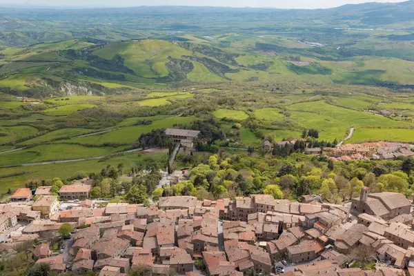 Geniş yeşil tepeler ve geleneksel Toskana köyü manzarası. Terracotta çatıları berrak bir gökyüzünün altındaki canlı manzarayla kusursuz bir şekilde harmanlanır. İtalya kırsalının pitoresk bir manzarası.