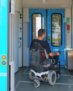 Erişilebilir tren yolculuğu kullanan tekerlekli sandalye kullanıcısı güneşli bir günde geniş tren girişinden geçerek modern şehirlerde kapsamlı ulaşım çözümlerinin önemini vurgular..