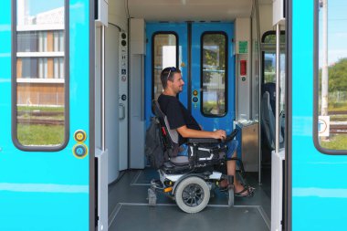 Özürlü bir adam nakil için trene biner. Tekerlekli sandalye kullanıyor ve gündüz vakti yolculuk için hazırlanıyor..