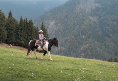 Kendine güvenen bir kovboy kızı sahnesinin özgün batı sahnesi. Hafif bir sis altında manzaralı dağ arazisinde at sürüyor.
