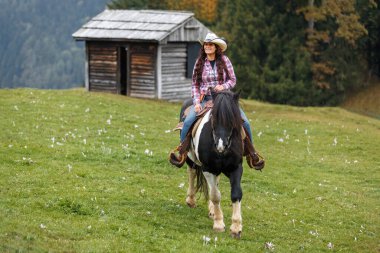 Kendine güvenen bir kovboy kızı sahnesinin özgün batı sahnesi. Hafif bir sis altında manzaralı dağ arazisinde at sürüyor.