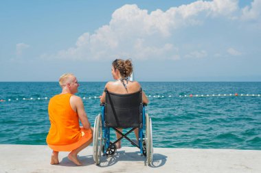Tekerlekli sandalyedeki engelli kadın cankurtaran yardımıyla deniz kenarında tatilin tadını çıkarıyor.