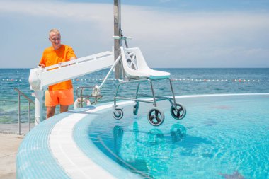 Yüzme havuzuna fiziksel engelli insanların girebilmesi için havuz sandalyesini kaldıran, kaldıran ve suya indiren bir adam..