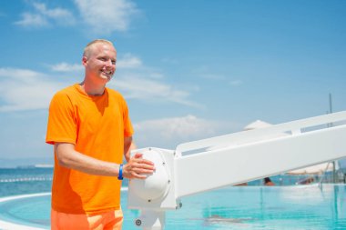Yüzme havuzuna fiziksel engelli insanların girebilmesi için havuz sandalyesini kaldıran, kaldıran ve suya indiren bir adam..