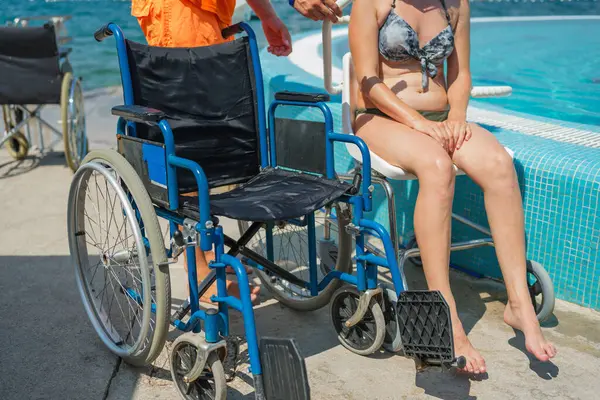 Deniz oteli cankurtaranı engelli bir kadına yardım ediyor erişilebilir hizmetler ve tesisler, havuz sandalyesi kaldırma, ve tekerlekli sandalye, tatil köyünde..