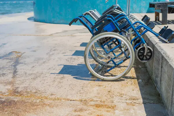 Engelliler için boş mavi çelikli tekerlekli sandalye, deniz kenarına yerleştirilir, güzel sahil çevresine erişim sağlanır..
