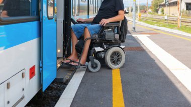 Tekerlekli sandalye kullanıcısı trene binmeye hazırlanırken tren istasyonunda yaklaşır. Güneşli bir gün, trene sorunsuz bir geçiş sağlıyor..