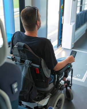 Engelli bir adam trendeyken tekerlekli sandalye kullanıyor.