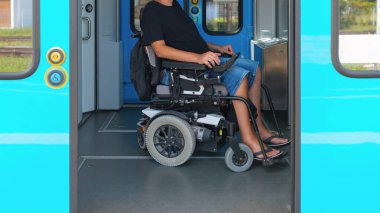 Erişilebilir tren yolculuğu kullanan tekerlekli sandalye kullanıcısı bir trenin kapısında bekliyor. Kolay erişim için tasarlanmış geniş iç mekanı gösteriyor. Kullanıcı günlük kıyafetlerle rahatlamış görünüyor.