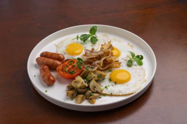 Kızarmış yumurta, sosis, ızgara domates ve beyaz tabakta servis edilen otlarla süslenmiş sotelenmiş mantarlarla nefis bir kahvaltı..