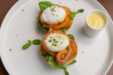 İki haşlanmış yumurta, somon ve taze yeşilliklerle birlikte kızarmış ekmeğin üzerinde servis edilir. Yanında da küçük bir bardak sos, kahvaltı için mükemmel olur..