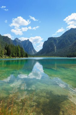 Toblacher 'ın berrak suları İtalya' daki parlak mavi gökyüzünün altındaki görkemli Dolomitleri yansıtıyor. Çamları çevreleyen çam ağaçları bu pitoresk yerde huzurlu atmosferi güçlendirir..