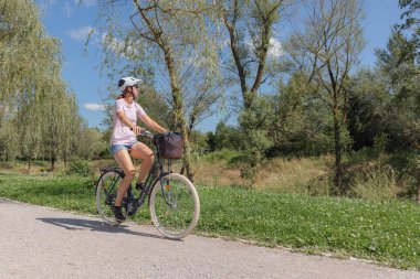 Parlak güneşli bir günde, verimli yeşillikler ve ağaçlarla çevrili çakıllı bir yolda sakin bir şekilde bisiklet süren bir insan, doğanın güzelliğinden keyif alır..