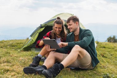 Modern genç çift kamp yapıyor, çadırlarının dışında eğleniyor, gülüyor, anları paylaşıyor ve şaşırtıcı bir doğal ortamda tablet üzerinde yayılıyor..