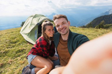 Çiftler, çadırlarının dışında fotograflarını çekerken, arka planda muhteşem dağ manzarası olan serin bir kamp anının keyfini çıkarıyorlar..