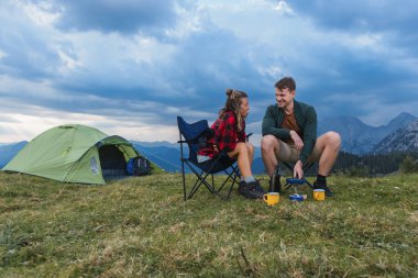 Genç bir çift, kaygısız bir kamp sabahının tadını çıkarıyor çadırlarının önünde eğleniyor, gaz ocağında krep yapıyor..