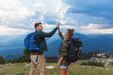 İki yürüyüşçü dağlarda keyifle vakit geçirir, bulutların ve zirvelerin muhteşem zeminine karşı beşlik çakarak yolculuklarını kutlarlar..