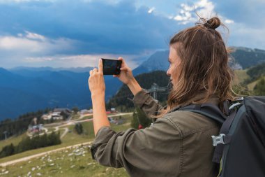 Yürüyüş yapan bir kadın, öğleden sonra saatlerinde doğa ve temiz havanın tadını çıkararak güzel dağ manzarasının fotoğraflarını çeker..