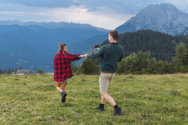 Gülümseyen kız arkadaşı tarafından yönetilen bir adam kamp alanının yanından geçerek nefes kesici bir dağ manzarasına doğru yürüyordu..