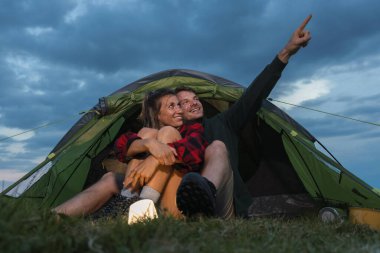 Bir çift çadırın içinde dinleniyor, sakin akşam atmosferinin tadını çıkarırken gökyüzünü işaret ediyorlar..
