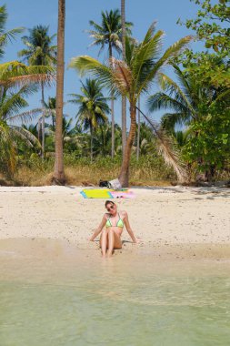 Bir kadın Tayland 'da tropik bir plajın kumlu sahilinde dinlenir. Palmiye ağaçları ve berrak mavi suyla çevrili, sıcak güneşin tadını çıkarıyor..