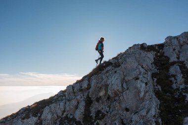 Kadın tırmanışçı gün doğarken engebeli bir dağ sırtına tırmanıyor, sabahın erken saatlerinde güneşleniyor ve temiz havanın tadını çıkarıyor..