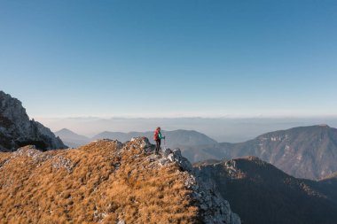 Yürüyüşçü kadın, nefes kesen vadiler ve uzak tepelerle çevrili kayalık bir dağın tepesinde güneşin doğuşunu yakalar..