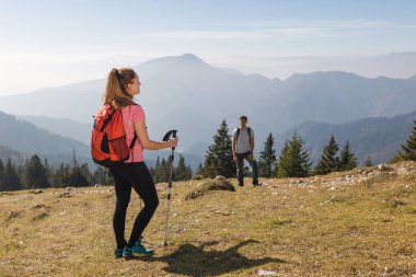 İki yürüyüşçü güneşli bir günde nefes kesen manzaralı bir dağ yolunu keşfederken mola verir..