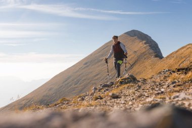 Kayalık arazi boyunca yürüyüş yapan bir insan, açık bir gökyüzü altında manzaralı dağ manzarasının tadını çıkarır..