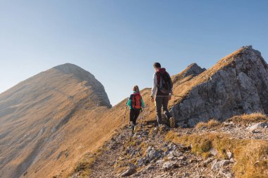 Aktif genç bir kadın ve bir erkek güneşli bir sonbahar gününde güzel bir dağ manzarasında yürüyüş yapıyorlar. Seyahat ve sırt çantası kavramları.