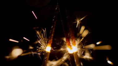 Karanlıkta üç kıvılcım parlıyor, bir kutlama sırasında etrafı ışıltılı ışıklarla aydınlatıyor..