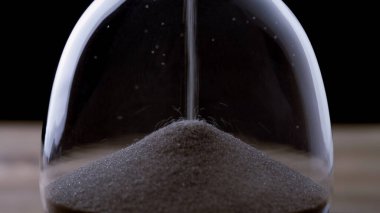 İnce kum, cam bir kum saatinde iniyor. Bu da zamanın sessiz ve odaklanmış bir anında geçtiğini gösteriyor..