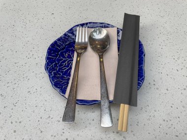 Seramik tabak, kaşık, çatal ve çubuklar gri masada. Akşam yemeği için Japon restoranı.