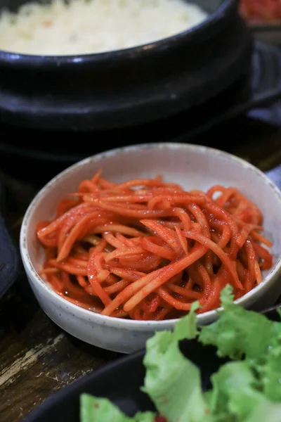 Korean traditional side dish made from papaya kimchi seasoning with hot chili pepper powder and sesame seeds on white dish wooden table
