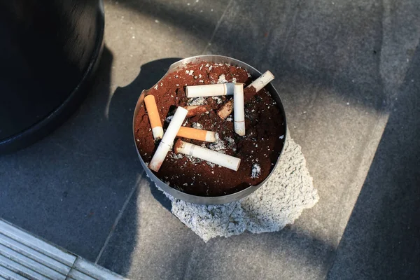 Ashtray with cigarettes butts under sunlight outdoor on street. Space for text. Unhealthy life style, Bad habits concept
