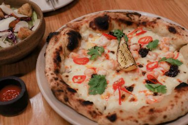 Yemek masasında lezzetli deniz ürünleri pizzası. Parmesan peyniri ve Mozzarella, zeytin ve limon. Fast food, konforlu yemek, İtalyan mutfağı konsepti