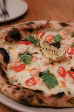 Yemek masasında lezzetli deniz ürünleri pizzası. Parmesan peyniri ve Mozzarella, zeytin ve limon. Fast food, konforlu yemek, İtalyan mutfağı konsepti