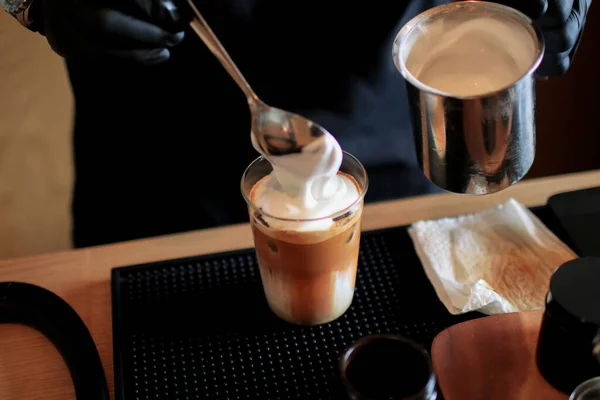 stock image Barista pour milk foam on Ice cappuccino coffee. Cold summer drink.  Cold summer drink on a dark wooden background with copy space.