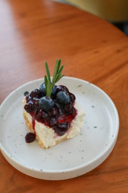 Beyaz tabakta yabanmersinli cheesecake. Kahve dükkanında taze pişmiş tatlının tadını çıkar. Dekoratif kekin yakın plan çekimi..