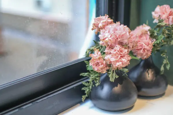 Pink flowers near window sill in living room. Home decoration with flowers and vase. Living room interior.