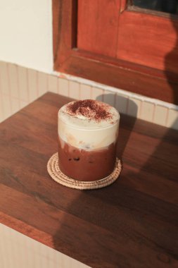 Sabah güneşinin altında köpüklü sütlü buzlu Mocha Coffee ve fotokopi alanı olan ahşap bir masanın üzerinde çikolata..