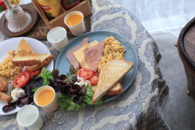 Amerikan kahvaltı yumurtası, jambon, sosis, pastırma, domates, ekmek ve salata. Sabahları sağlıklı besleniyorlar..