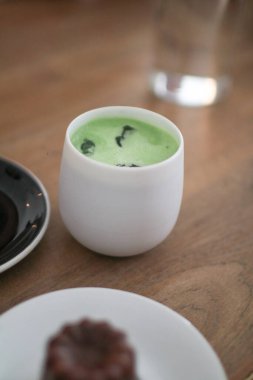 Cafe 'deki ahşap masada yeşil çay, sütlü latte. Japon geleneksel seramik kasesi. Çeşit çeşit tatlı fırın ve pastane-