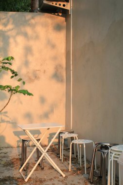 Sabah güneş ışığı altında beyaz masa ve sandalye. Bahçede rahat bir çatı katı tarzı. Modern ve canlı mobilya dekorasyonu.