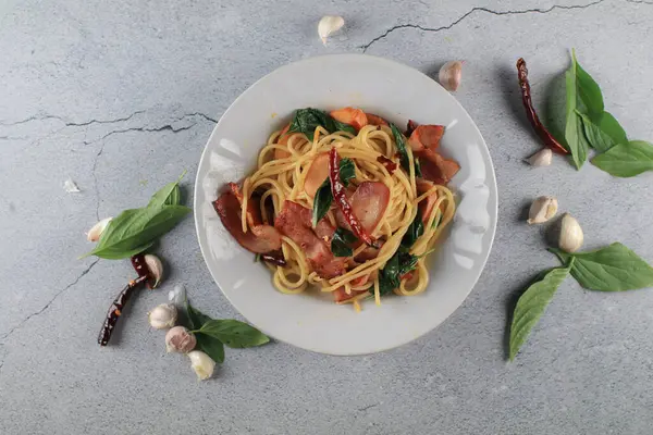 Pastırmalı spagetti biberli sarımsaklı fesleğen ve gri arka planda beyaz tabak. Popüler menü klasik İtalyan mutfağı. Lezzetli baharatlı yemekler..