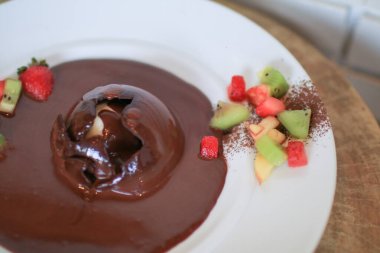 Çilek ve kiviyle süslenmiş çikolata kubbesinin üzerine çikolata sosu dökülüyor. Lezzetli taze tatlı.
