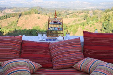 Kırmızı yastıklı ikindi çayı Tayland tarzı ipek desenli ve dağ manzaralı sabahları. Dışarıda, balkon terasında. Tatilde seyahat.