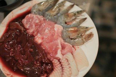 Domuz dilimleri ve karides soslu shabu. Tayland usulü güveç. Çiğ et, beyaz tabakta sukiyaki sosu. Tatil köyündeki gezginler için akşam yemeği..