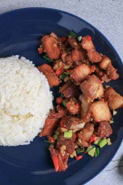 Kırmızı biberle pişirilmiş domuz eti ve siyah tabakta pirinçli sarımsak. Asya yerel sokak yemekleri tarzı.