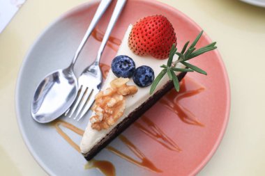 Seramik tabakta koyu bira keki ve çilek, yabanmersini, biberiye ve fıstık ile süslenmiş..